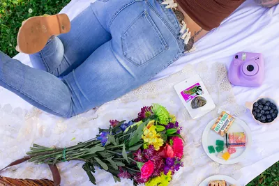 Picnic blanket flat lay with flowers, a camera and Best Buds products